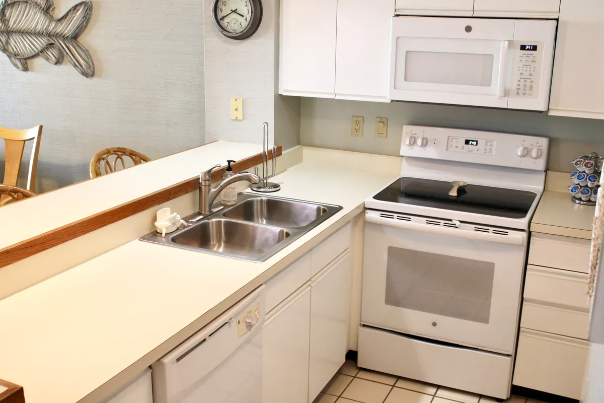 A warm, inviting kitchen scene with a visible stove, microwave, kitchen sink, dining chairs, and a wall clock. The space exudes a homey feel, ideal for cooking, baking, and socializing.
