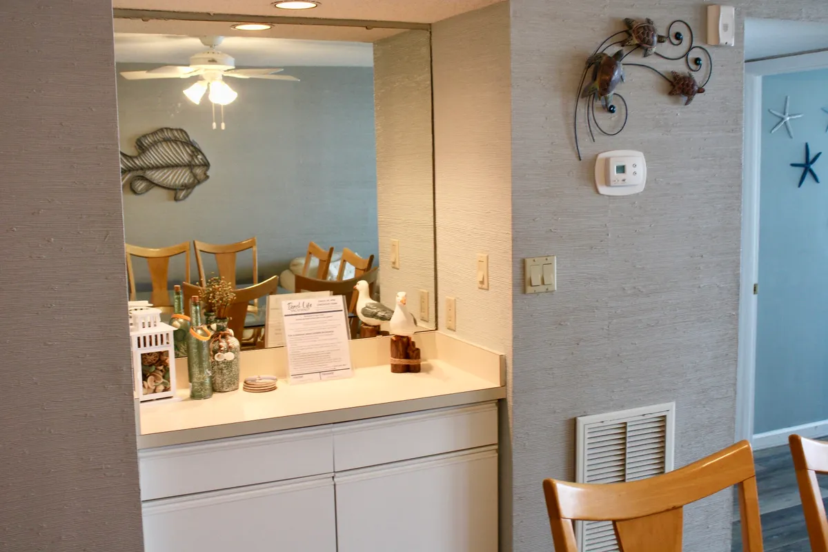 A relaxed dining and kitchen area featuring a kitchen island surrounded by dining chairs, decorative fish accents, and a large mirror. The setting is open and welcoming, perfect for social dining and group gatherings.